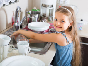 young girl smiling and doing dishes